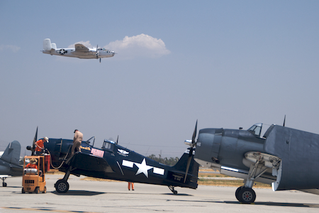 A B-24 Liberator comes in for a low pass while some guys work on an F6F Hellcat that claims to have shot down 29 Japanese planes, despite being in something called the "Commemorative Air Force".