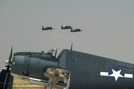 Three aerobatic F8F Bearcats fly in formation, shaming one of their less well-heeled bretheren into folding up its wings.